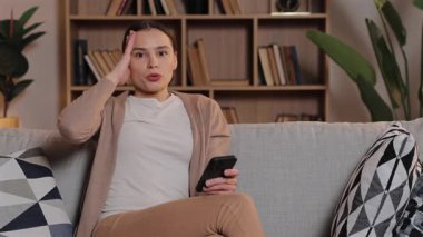 Kafkasyalı bir kadın kanepeye oturmuş elinde akıllı bir telefonla Temple 'a dokunuyor. Hayal kırıklığı gösteriyor. Evde, rahat bir odada, arkada kitaplarla derin bir nefes alıp verirken, sinirini dışa vuruyorsun..