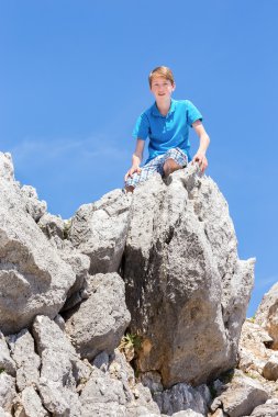 Kayalar üzerine oturan beyaz genç çocuk
