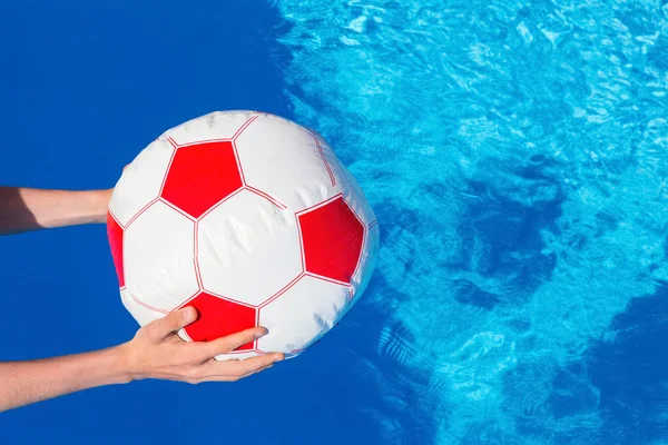 Braccia che tengono la palla da spiaggia sopra l'acqua della piscina — Foto Stock