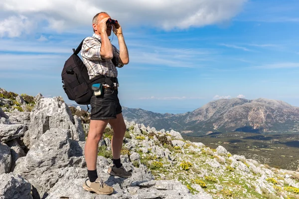 European man on rocks looking through binoculars — Stock Photo, Image