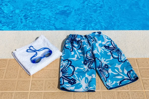 Swimming trunks goggles and towel at pool