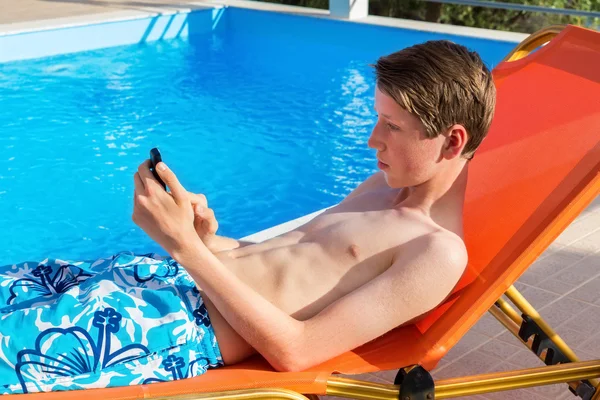 Youngster operating mobile phone at swimming pool — Stock Photo, Image