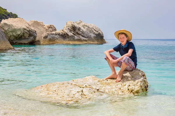 Ragazzo con cappello seduto sulla roccia in mare — Foto Stock