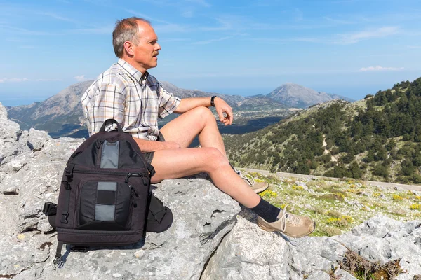 Caucasian man sitting with backpack in greek mountains — Stock Photo, Image