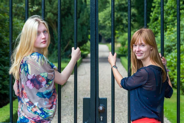 Twee meisjes houden van metalen staven van toegangspoort. — Stockfoto