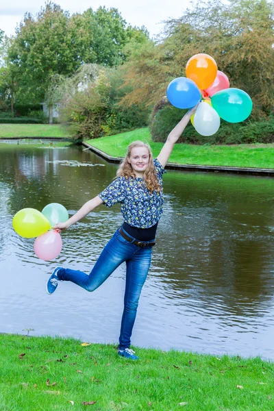 Girl standing at pond with colored balloons — Stock Photo, Image