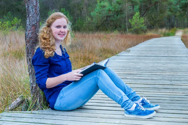 Nederlandse meisje het lezen van boek op houten wandelpad in bos — Stockfoto