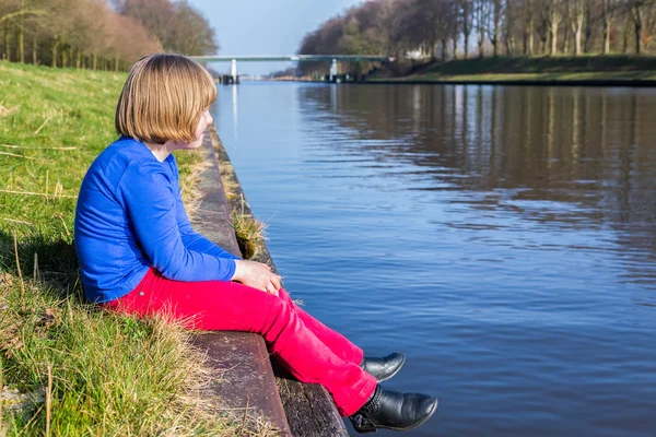 Young girl sitting at waterfront of canal — Stock Photo, Image