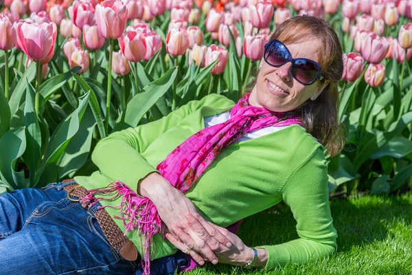 Mujer acostada frente al campo de tulipanes rosa — Foto de Stock