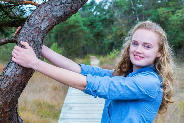 Blond holandské dívka drží kmen stromu v přírodě — Stock fotografie