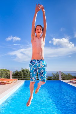 Dutch teenage boy jumping high above blue swimming pool