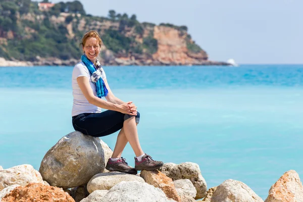 European woman as tourist sitting on rocks near blue sea — Stockfoto