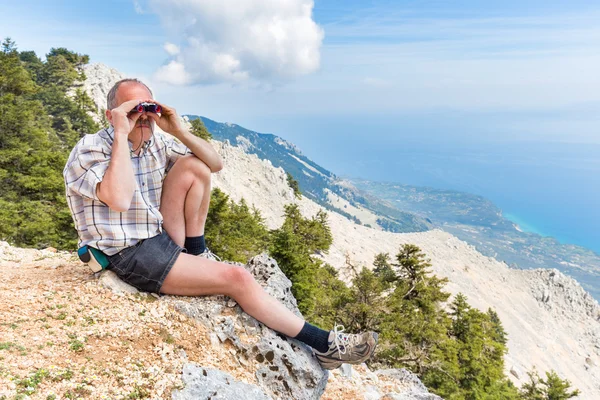 Dutch man sitting in mountains looking through binoculars — Stock Photo, Image