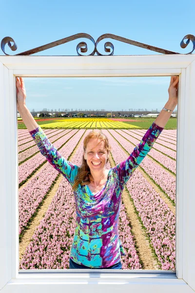 Holländerin steht im Fenster vor rosafarbenem Blumenfeld — Stockfoto
