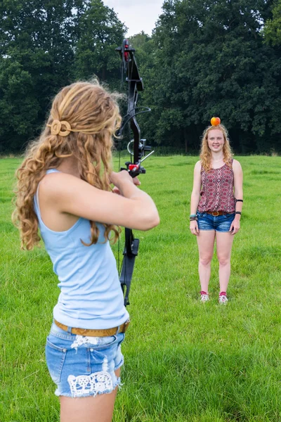 Fille visant flèche de l'arc composé à la pomme sur la tête de la femme — Photo