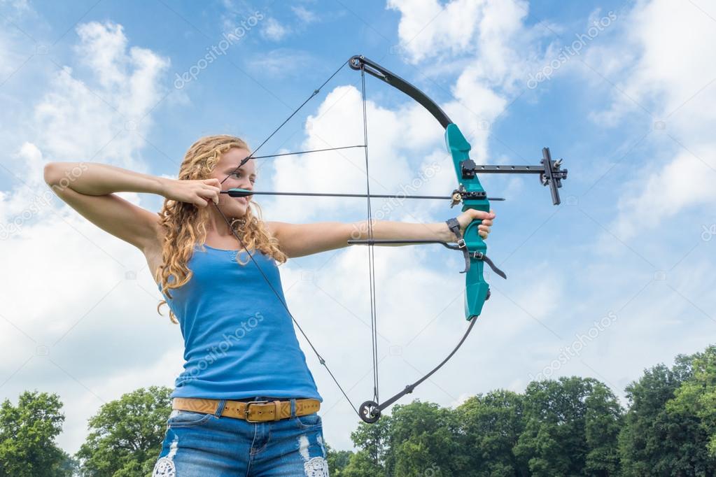 Blonde caucasian girl shooting with arrow and compound bow