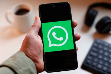 VALENCIA, İSPA 01.27, 2026: Bir el, modern bir çalışma ortamında mobil mesajlaşma, bağlantı ve dijital iletişimi öneren canlı yeşil ekranda hat logosunu gösteren bir akıllı telefonu kavrıyor.