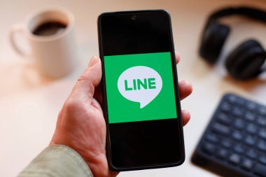 VALENCIA, İSPA 01.27, 2026: Bir el, modern bir çalışma ortamında mobil mesajlaşma, bağlantı ve dijital iletişimi öneren canlı yeşil ekranda hat logosunu gösteren bir akıllı telefonu kavrıyor.