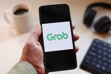 VALENCIA, SPAIN 01.27, 2026: Bir kullanıcı BMW APP logosunu bulanık arka planda kahve fincanı ve klavyesi, taşınabilir teknoloji, marka kimliği ve premium otomotiv markası ile mavi ekranda gösteren bir akıllı telefon tutar