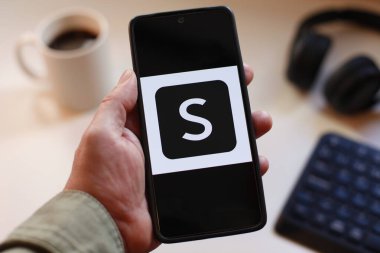 VALENCIA, SPAIN 01.27, 2026: Bir kullanıcı BMW APP logosunu bulanık arka planda kahve fincanı ve klavyesi, taşınabilir teknoloji, marka kimliği ve premium otomotiv markası ile mavi ekranda gösteren bir akıllı telefon tutar