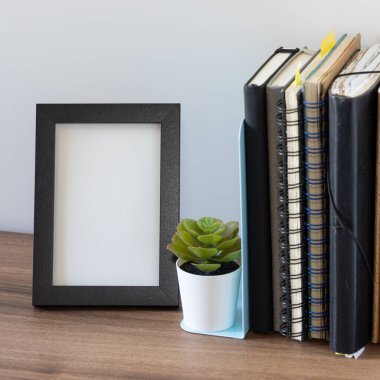 Boş siyah fotoğraf çerçevesi, dizüstü bilgisayarların ve ahşap yüzeyde küçük, sulu saksıların yanında. Ev dekorasyonu, iç tasarım, hafıza gösterimi ve model şablonlar için mükemmel.