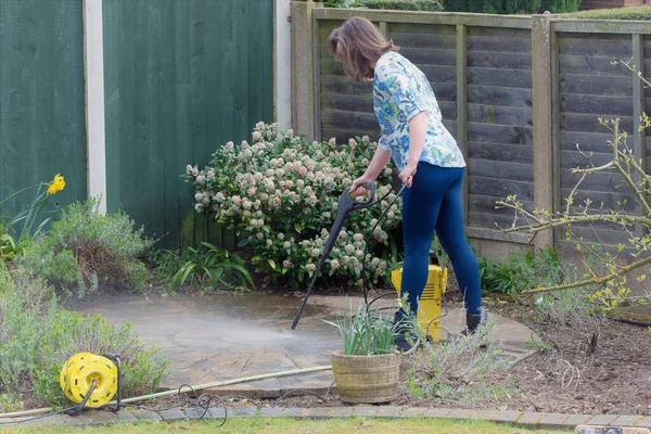 An energetic woman uses a power washer to transform a black coloured stone circle to its original red brick colour, by removing engrained dirt from the surface.