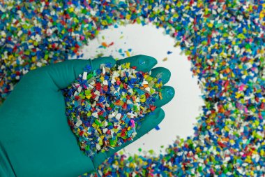Yeşil eldivenli, ezilmiş plastik. Plastiğin yeniden kullanımı. polimer boncuklar. Plastik atıktan elde edilen kırıntılar. Dünyanın plastik azaltma politikası. Beyaz arkaplandaki plastikleri temizler.