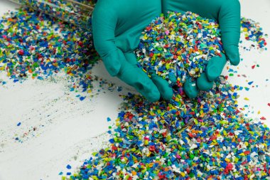 Yeşil eldivenli, ezilmiş plastik. Plastiğin yeniden kullanımı. polimer boncuklar. Plastik atıktan elde edilen kırıntılar. Dünyanın plastik azaltma politikası. Beyaz arkaplandaki plastikleri temizler.