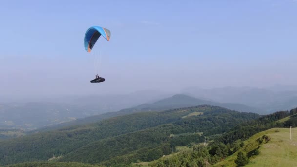 Luchtfoto van een parachute die hoog boven het groene berglandschap vliegt — Stockvideo