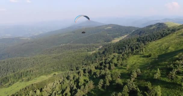 Вид с воздуха на парашют над зелеными горными холмами — стоковое видео