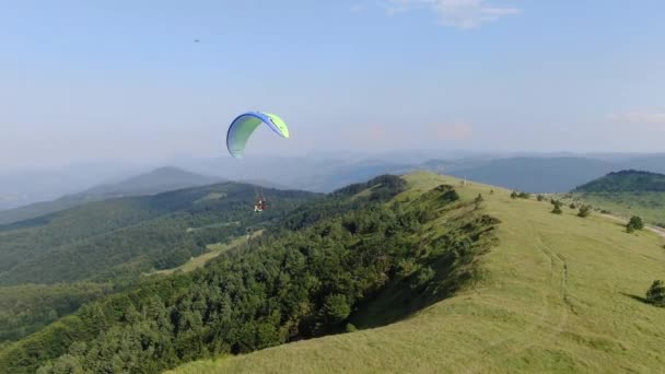 Spadochronowy spadochron lecący nad zielonym górskim krajobrazem. Widok z lotu ptaka — Wideo stockowe