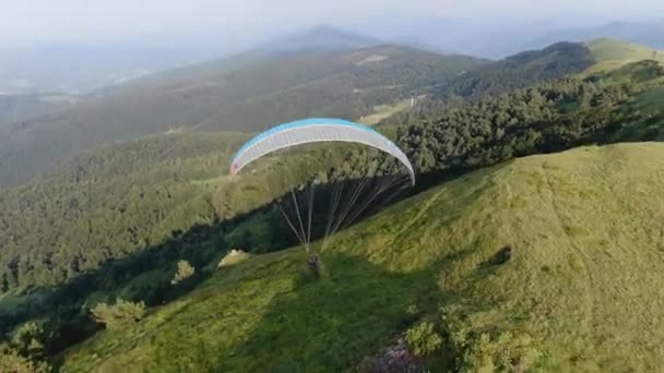 Отслеживание воздушного вида парапланеризма Пакархута, летящего над зелеными горными холмами — стоковое видео