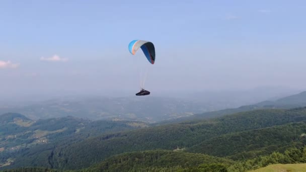 Вид с воздуха на парашют с двумя людьми, летящими над зелеными холмами — стоковое видео