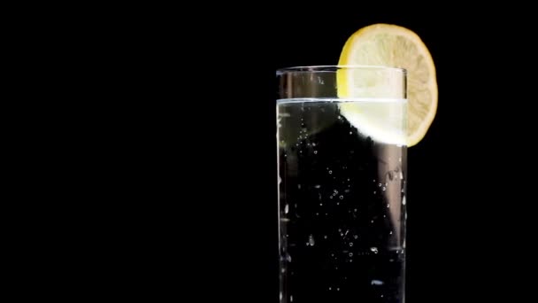 Αφρώδες νερό με σφήνα λεμονιού Περιστροφή σε απομονωμένο μαύρο φόντο — Αρχείο Βίντεο