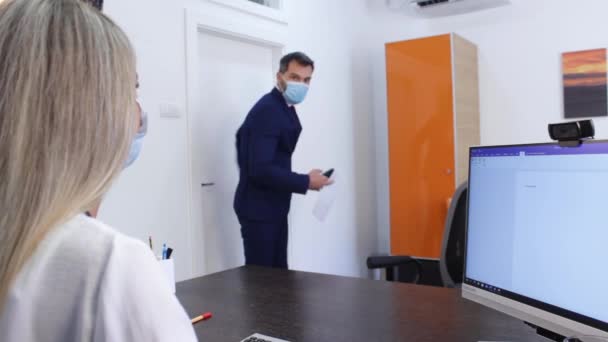 Бизнесмен в маске с бумагами, входящий в офис с женщиной-сотрудником — стоковое видео