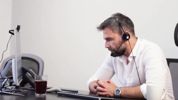 男子与耳机在现代办公室在电脑屏幕前呼叫，静态 — 图库视频影像