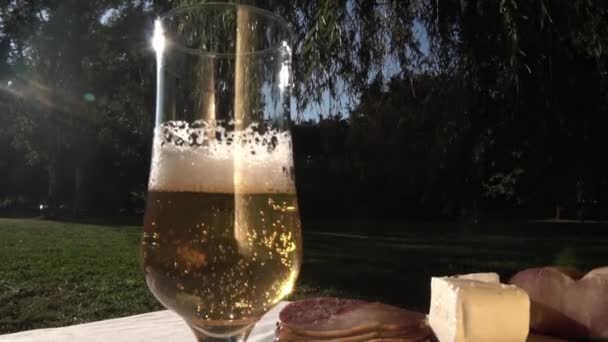 Glas av öl på utomhus picknickbord med en reflektion, ost och Prosciutto — Stockvideo