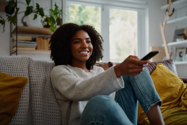 Portret van een vrolijke vrouw zittend op de bank thuis tv kijken en afstandsbediening vasthouden — Stockfoto