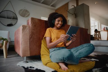 Evde kulaklıklı dijital tablet kullanarak rahatlarken neşeli genç bir kadının video izlediği düşük açı.