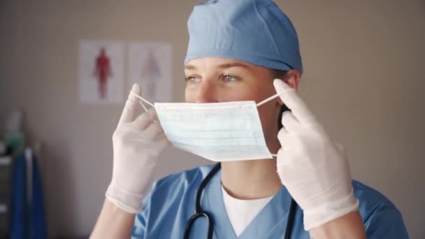 Fisioterapeuta profissional feminina em luvas cirúrgicas e boné usando máscara protetora para se proteger do coronavírus — Vídeo de Stock