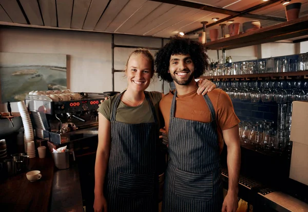 Young cafe owners wearing apron standing behind counter in cafe looking at camera — Stock Photo, Image