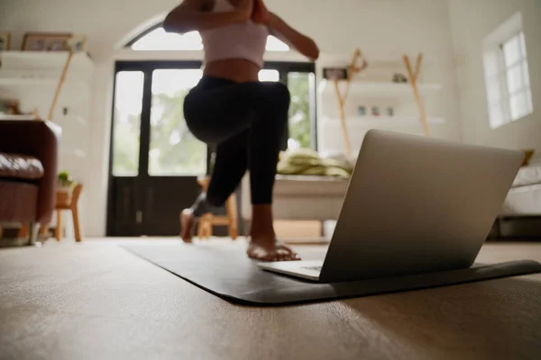 Крупним планом ноутбук на фітнес-мат з молодою жінкою, що практикує вправи з йоги за допомогою онлайн-відео — стокове фото