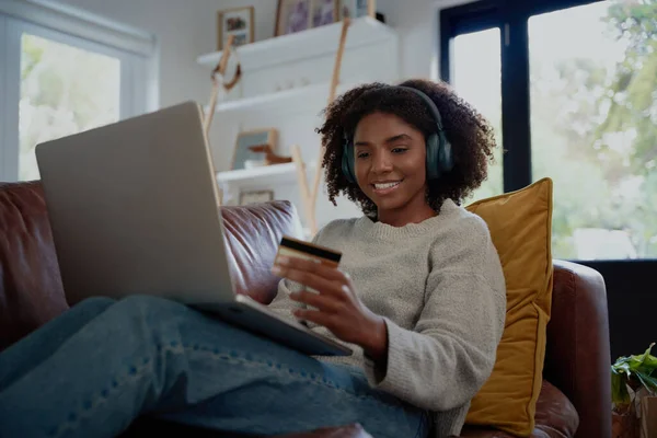 デビットカードとラップトップを使用してオンライン取引を行うBluetoothヘッドフォンで音楽を聴く幸せな女性 — ストック写真