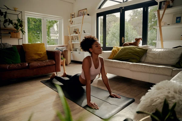 Mulher africana deitada no tapete de ioga em casa fazendo exercício de alongamento — Fotografia de Stock