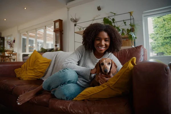 Retrato de mulher negra brincando com cão dachshund animal de estimação em casa sentado no sofá — Fotografia de Stock