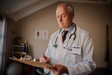 Erkek doktor hastanedeki panoya notlar yazıyor.