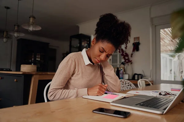 Young female entrepreneur holding neck due to pain while working on laptop with diary and document at home