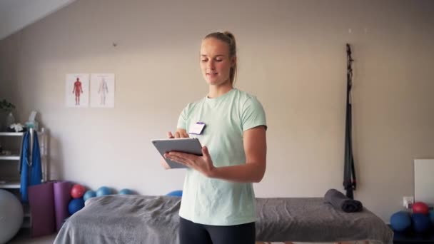 Tiro de um belo sorriso loira jovem fisioterapeuta usando tablet digital no centro de reabilitação — Vídeo de Stock