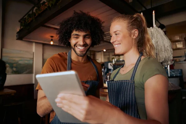 Ritratto di colleghi di sesso maschile e femminile che indossano grembiule e ridono mentre guardano il video in tablet digitale nel caffè — Foto Stock