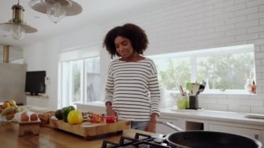 Mutlu genç Afrikalı kadın modern mutfakta tahta kesme tahtasıyla kırmızı biber dilimliyor.